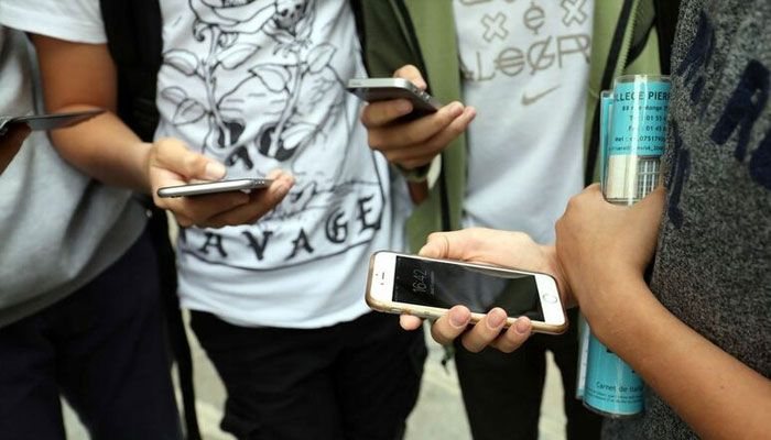 Teenagers standing together, looking at their smartphones